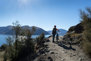 Fototapeta premium Tourist pushing the bike uphill on Glendhu Bay track along Lake Wanaka, South Island.
