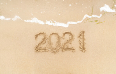 The year 2021 is written on a sandy beach with sea foam. The concept of the outgoing year, the new year