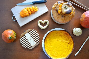 Overhead view of a table with a roasted pumpkin, a piece of pumpkin on a table, paper pumpkins, candies, a pumpkin with a witch hat and a pumpkin pie prepared for Halloween