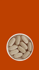 white medical pills on orange background vertical copy space. dietary supplements close-up. wellbeing and personal health care concept top view