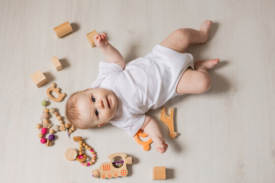 charming baby in white bodysuit lies on his back on the floor among rattles and wooden educational toys. top view. High quality photo