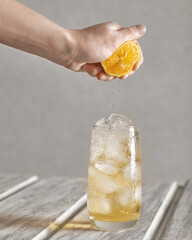 a woman's hand squeezes a lemon into a glass of refreshing homemade lemonade with ice