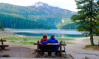 Couple sitting on a bench. Black Lake or Crno Jezero. National park Durmitor 
