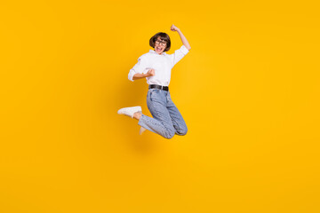 Fototapeta na wymiar Photo of astonished successful lady jump rejoice wear specs white shirt jeans sneakers isolated yellow color background
