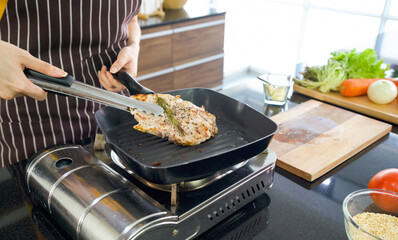 Chef uses tongs to tong the steak from the hot pan. The wooden chop board full of various kinds of vegetables are on the counter.