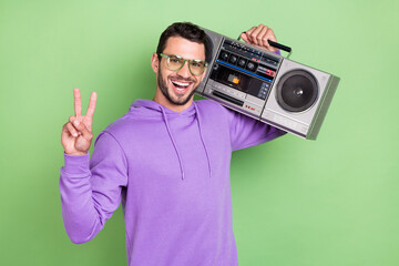 Photo of funky young brunet guy hold boom box wear spectacles hoodie isolated on green color background © deagreez