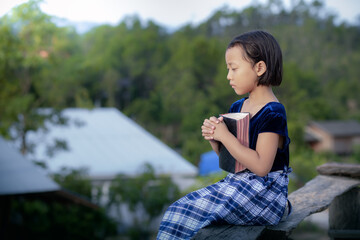 Asian little girl holding Bible and praying in morning with copy space, christian concept.