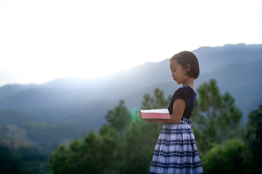 Cute little girl reading bible on mountain sunlight with copy space, christian concept.