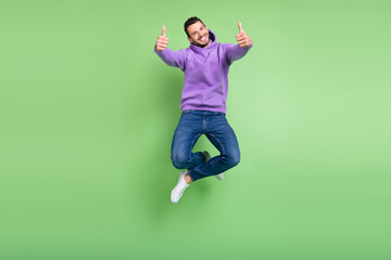 Full size photo of cool young brunet guy jump show thumb up wear hoodie jeans sneakers isolated on...