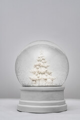 A white Christmas snow globe with white Christmas tree decorated with presents and gifts. White...