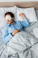 Top view of man in mask and pajama sleeping on bed
