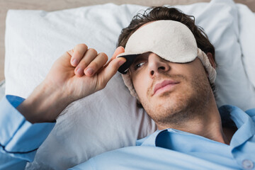 Young man in pajama and sleep mask lying on bed