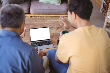 Biracial adult son and senior father holding cups of coffee and making laptop video call