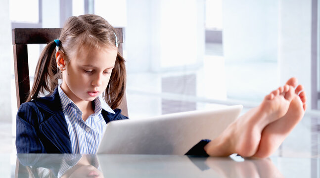 Humorous image of business child girl with bare feet on the table is working in office after lockdown. Selective focus on  bare feet. Horizontal image.