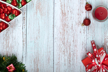 Christmas dinner table decorations with chocolate candies, scented candles and a red gift box.
