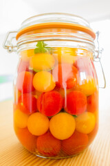 Lacto-fermented vegetables, tomatoes cherries. Vegetarian and vegan probiotics food. Glass jar on wooden kitchen table with light background. France.