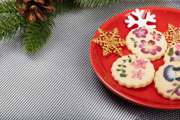 Beautiful edible flower cookies with Christmas ornament snowflakes on a bright red plate.