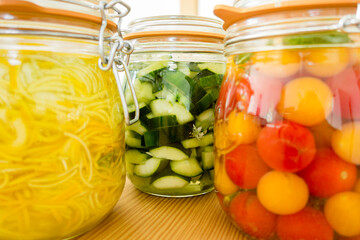 Lacto-fermented vegetables, cherries tomatoes, zucchini and cucumber. Vegetarian and vegan probiotics food. Glass jar on wooden kitchen table. France.