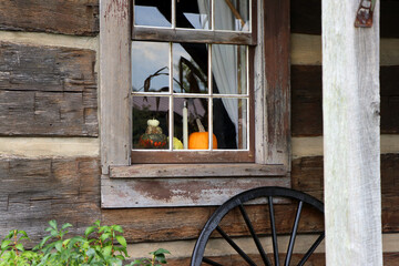 A log cabin window is decorated for the fall season with pumpkins. - obrazy, fototapety, plakaty