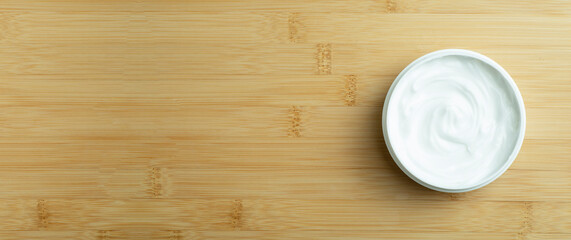 Cosmetic cream banner background. White cosmetic cream for skin and body in an open white jar on a wooden bamboo empty background. Copy space