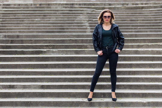 Cool portrait of a woman in black clothes on the steps of a city staircase. Free and independent woman concept