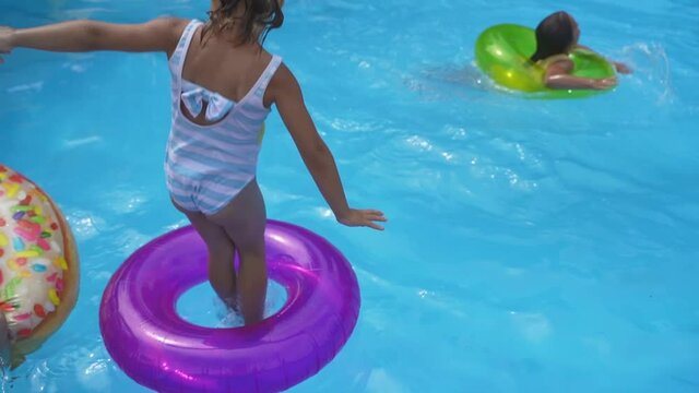 Funny little girls sisters jumps into an inflatable circle with a pool side. happy Children have fun and play, dives on the water pool in the swimming ring in summer on vacation, holidays, weekends