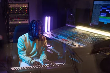 Tuinposter African musical producer playing electric piano and writing music in the recording studio © AnnaStills