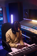 African young composer in headphones playing piano to write music in the recording studio