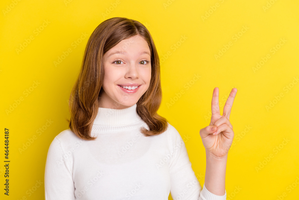 Poster photo of attractive young positive little girl smile make v-sign hello good mood isolated on yellow 