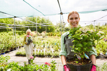 Woman as a gardener apprentice with flowers in the greenhouse