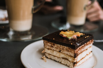 Close-up of delicious chocolate cake on white plate. Tasty dessert in cafe or restaurant. Couple of glasses of coffee in background.