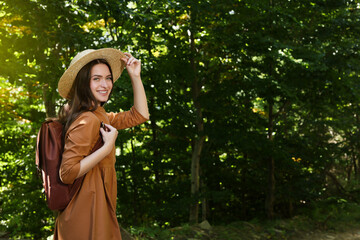 Fototapeta premium Happy woman with backpack and hat enjoying her walk in forest