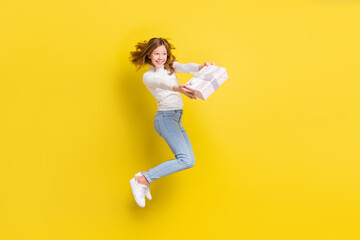 Fototapeta na wymiar Full length photo of happy brown haired little girl jump up hold hands gift box isolated on yellow color background