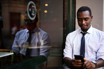 African businessman drinking coffee in cafe. Happy smiling man using the phone