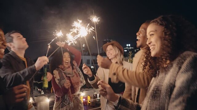Diverse group of friends having a good time and dancing with sparklers outdoors in the night time. High quality 4K footage 
