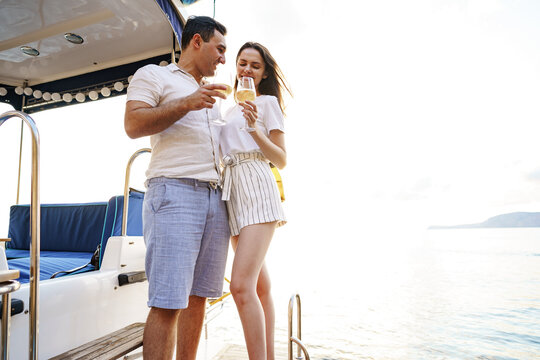 Young loving couple sitting on the yacht deck and drinking wine