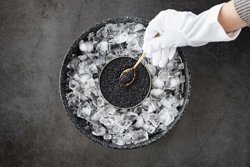 Fototapeta na wymiar hand of waiter in gloves take a black caviar in spoon