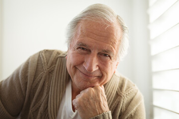 Portrait of smiling senior caucasian man looking at camera and touching his chin at home