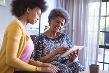 Smiling african american senior woman with adult daughter using tablet
