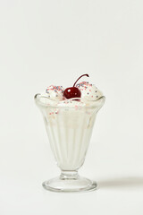 Vanilla sundae ice cream in cup with sweet grains and bing cherry on top isolated on white background