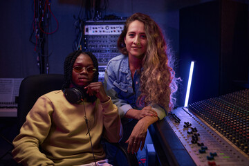 Portrait of young singer with her musical producer looking at camera while working in digital recording studio