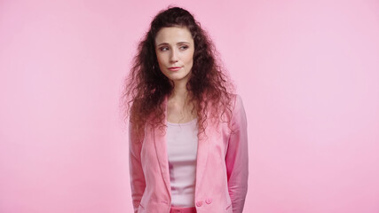 brunette and curly young woman looking away isolated on pink