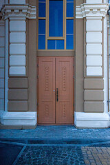 Vertical photo of a wooden door of a beige and white building