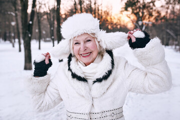 Obraz premium senior woman in white hat and fur coat enjoying winter in snow forest. Winter, age, season concept