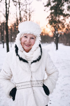 senior woman in white hat and fur coat enjoying winter in snow forest. Winter, age, season concept