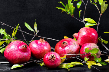 red pomegranates with green leaves on wooden old cutting board, side view, dark background