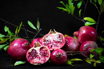 red pomegranates and seeds with green leaves on wooden old cutting board, side view, dark background