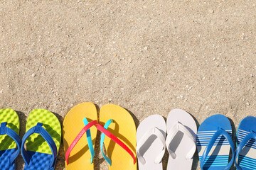 Many different flip flops on sand, flat lay. Space for text