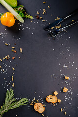 Dark background for the menu on which large salt, vegetables, spices, rosemary and cherry tomatoes are scattered.