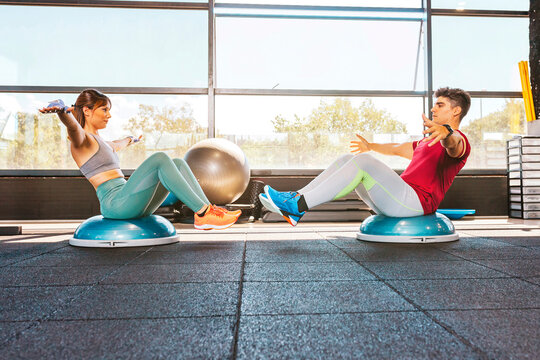 Couple doing exercises on the bosu abdominal muscles during workout at gym. Workout with personal trainer. Physical exercise concept.
